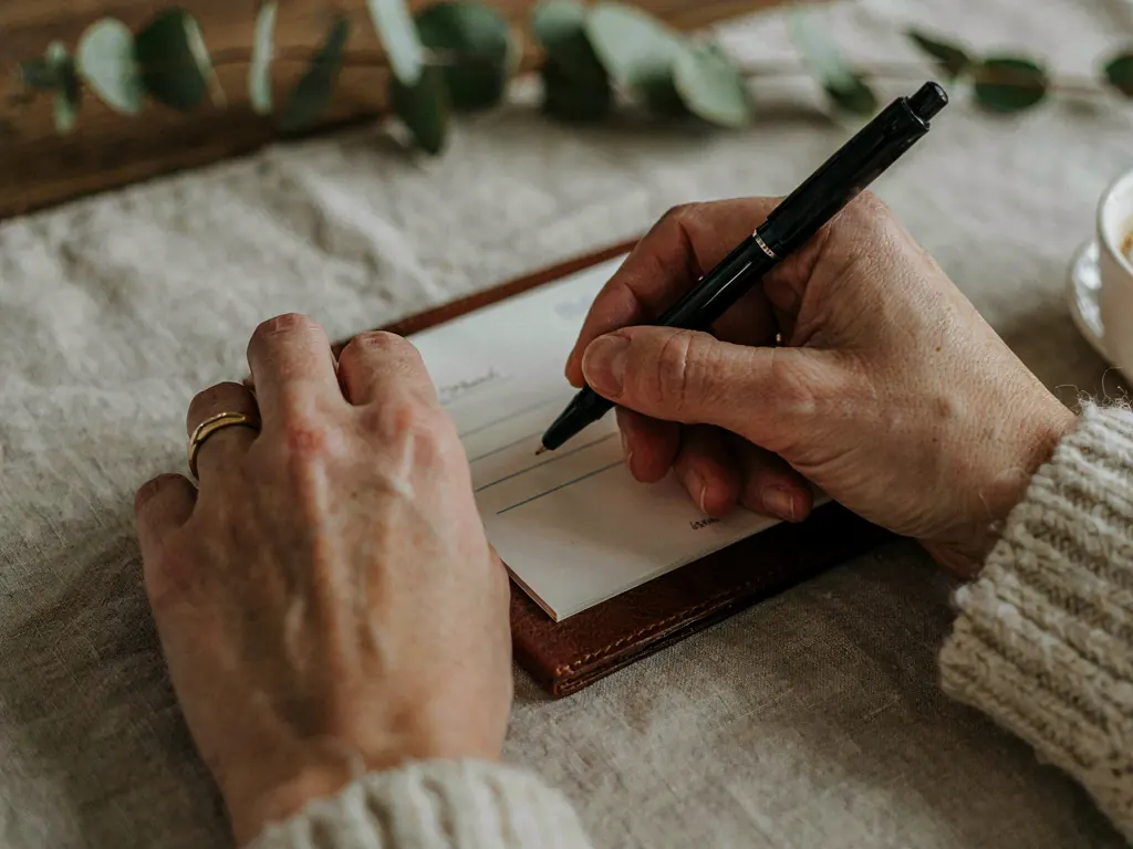 Two hands writing a check in a leather checkbook on a linen tablecloth