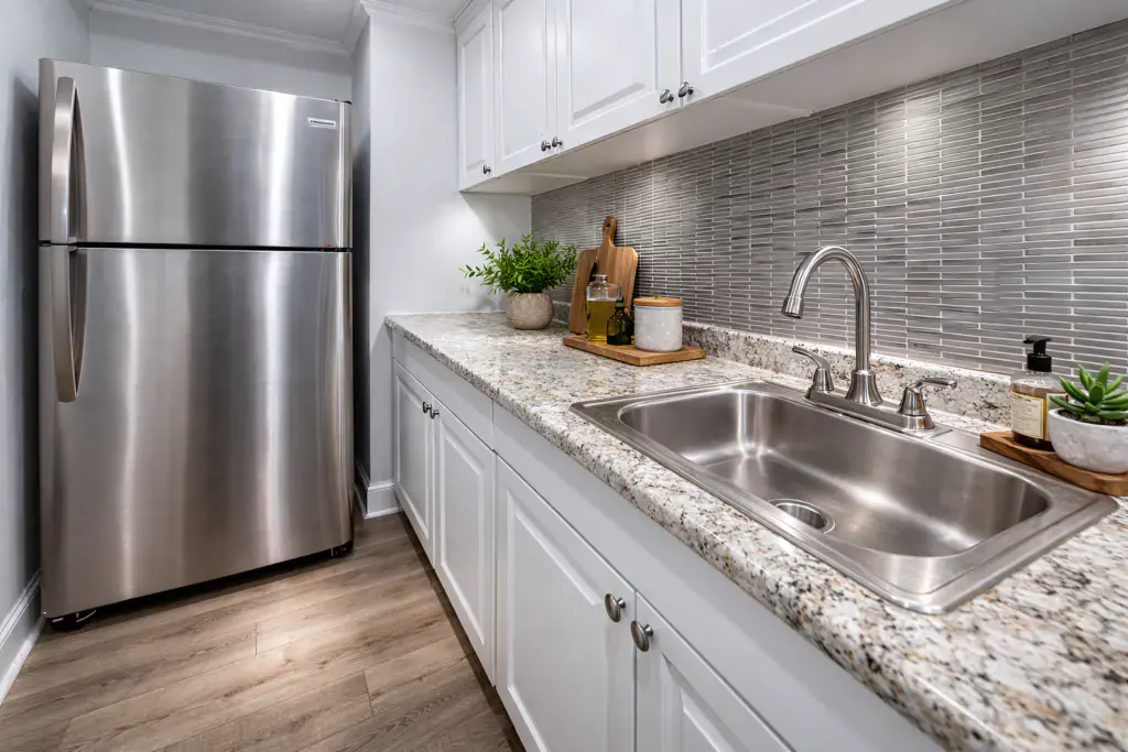 Renovated galley kitchen with white cabinets, granite counters, a stainless refrigerator and a tiled backsplash